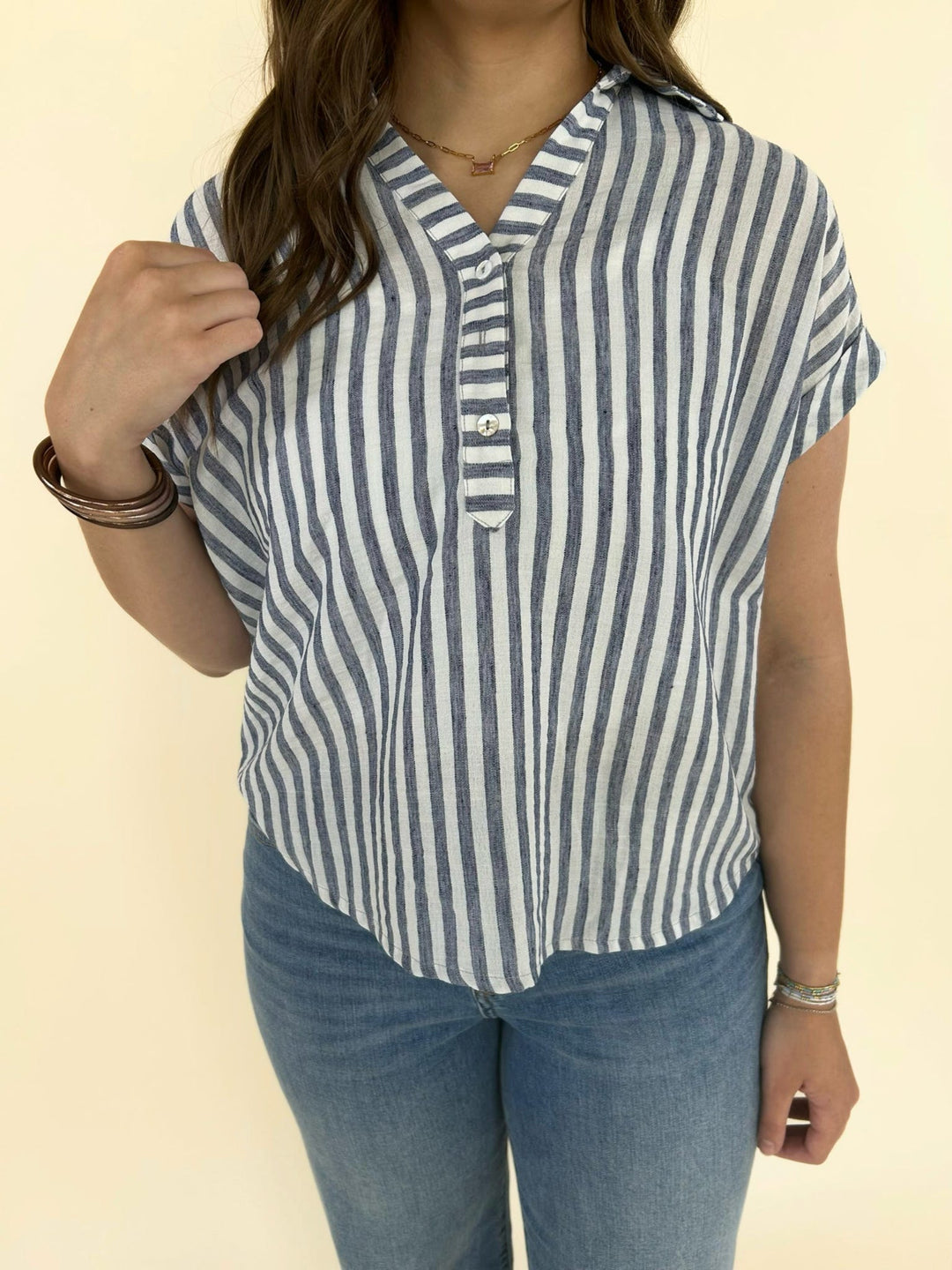 Front view of blue and white vertical striped button front blouse with short sleeves and relaxed fit paired with denim jeans