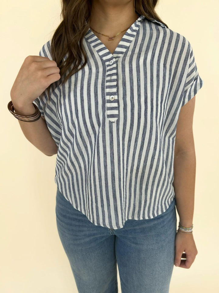 Front view of blue and white vertical striped button front blouse with short sleeves and relaxed fit paired with denim jeans
