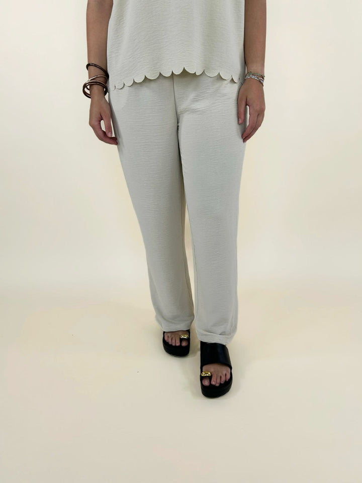 Front view of women’s cream wide leg pants with scalloped hem top set and black slide sandals