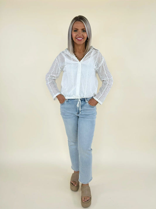 Full body front view of white long sleeve eyelet blouse with drawstring hem styled with light wash cropped jeans and platform sandals
