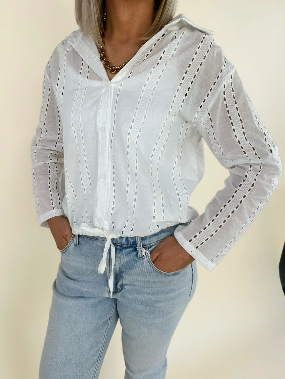 Close up front detail of white eyelet blouse with button front, lightweight fabric, and adjustable drawstring hem