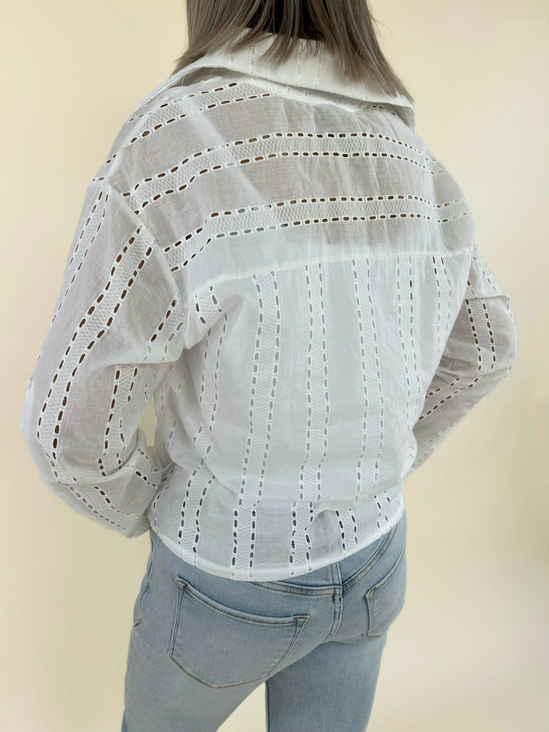 Back view of white long sleeve eyelet blouse featuring sheer textured fabric and relaxed silhouette with light wash jeans