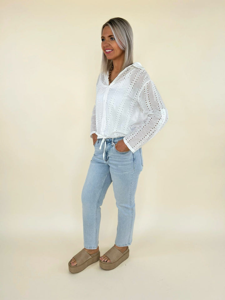Side view of white eyelet long sleeve blouse with relaxed fit and drawstring waist paired with light wash denim jeans
