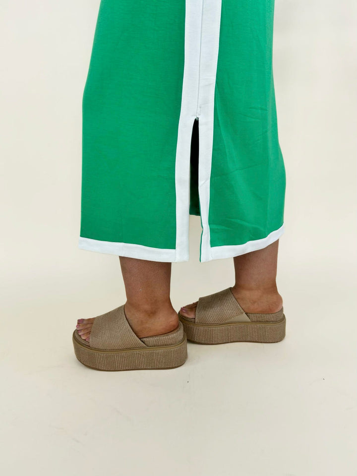 Close-up of green midi dress hem with white trim and side slit detail paired with tan platform sandals