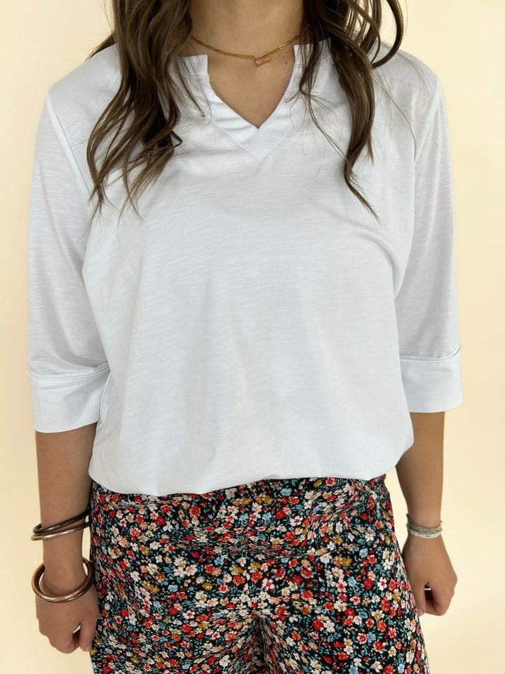 White V-neck blouse with 3/4 sleeves paired with black floral wide-leg pants, front detail view women’s boutique outfit