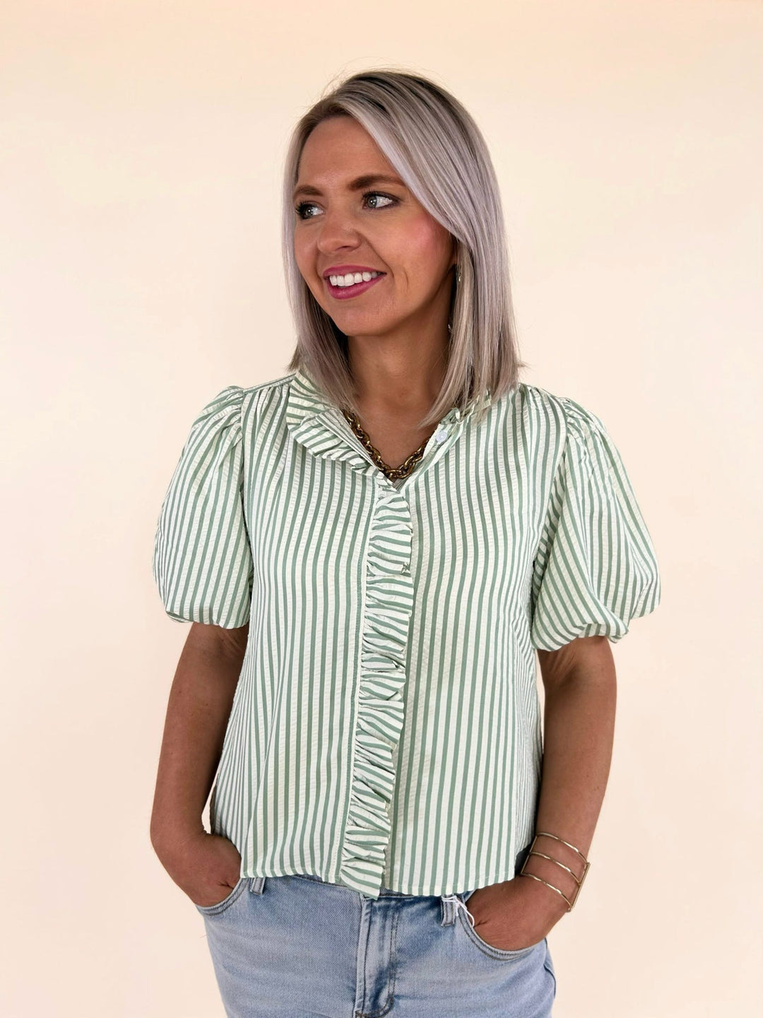 Front close-up of green striped ruffle blouse with button front detail and puff sleeves, styled with light wash denim