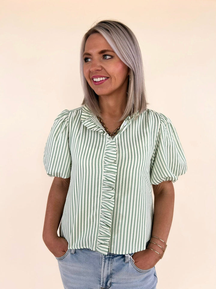Front close-up of green striped ruffle blouse with button front detail and puff sleeves, styled with light wash denim