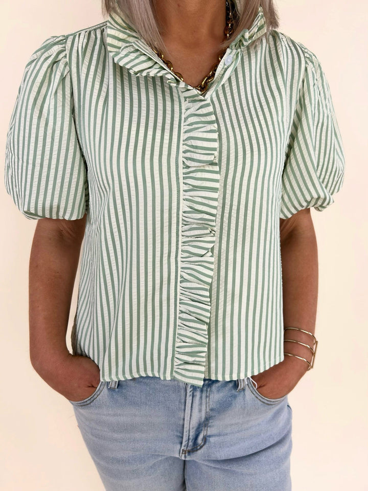 Detailed front torso view of green and white striped blouse highlighting ruffle placket and vertical stripes with light wash jeans