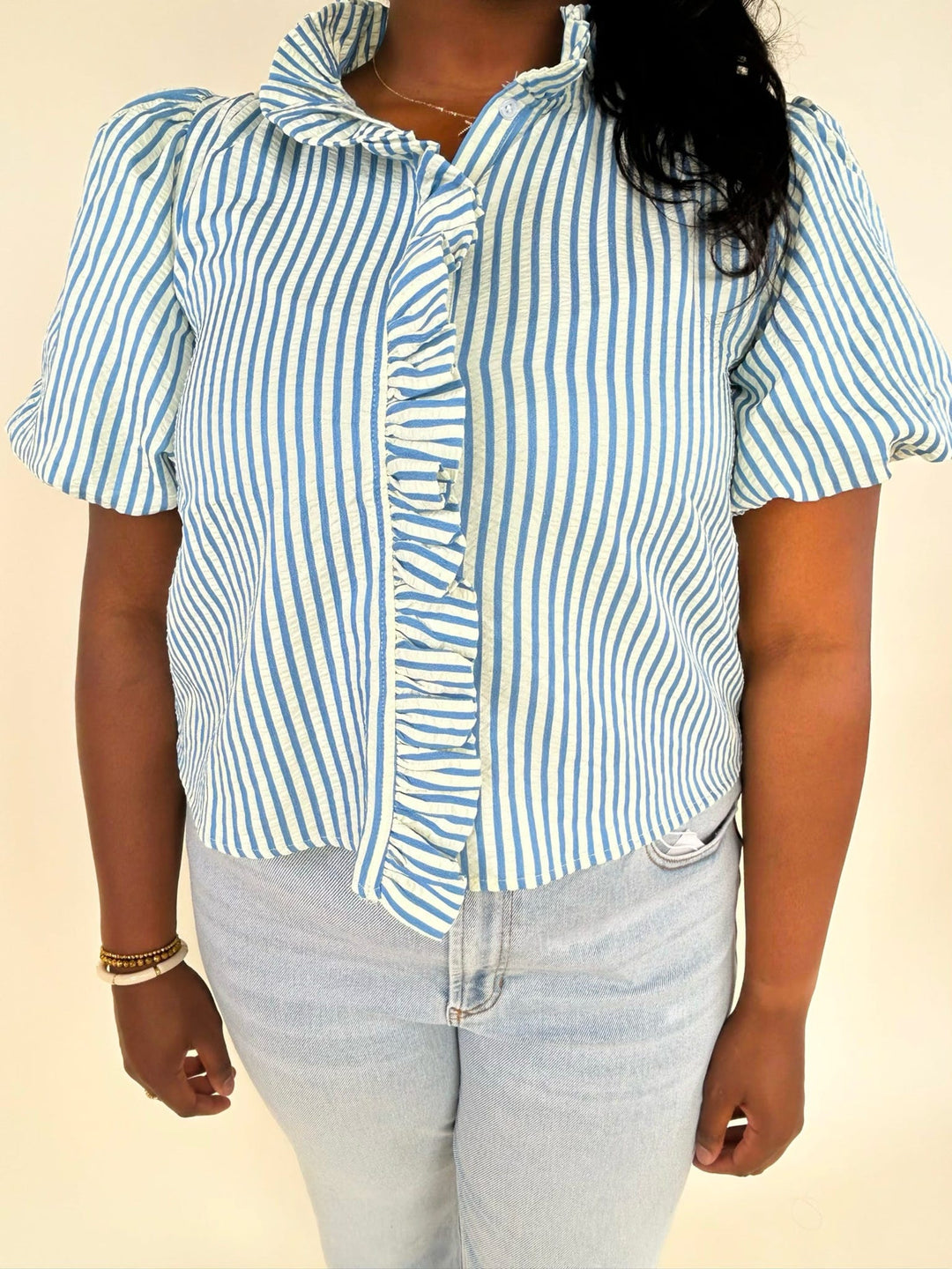 Detailed front view of blue and white striped blouse with ruffle placket and puff sleeves, paired with light wash jeans