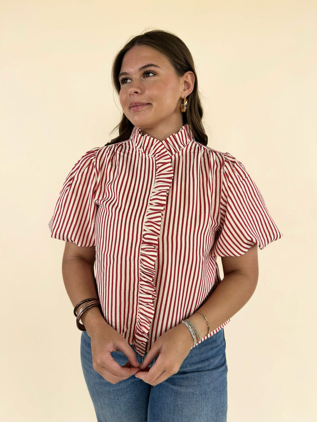 Front upper view of red and white striped ruffle blouse styled with wide leg jeans and gold accessories