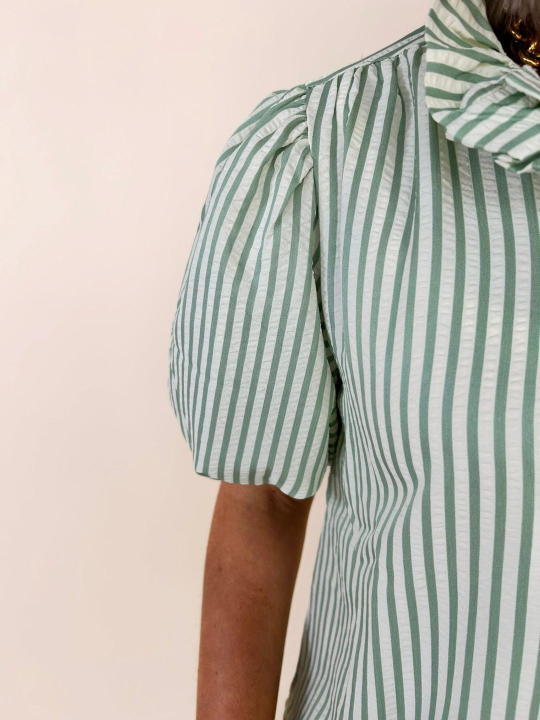 Close-up sleeve detail of green striped blouse showing puff sleeve structure and textured stripe fabric