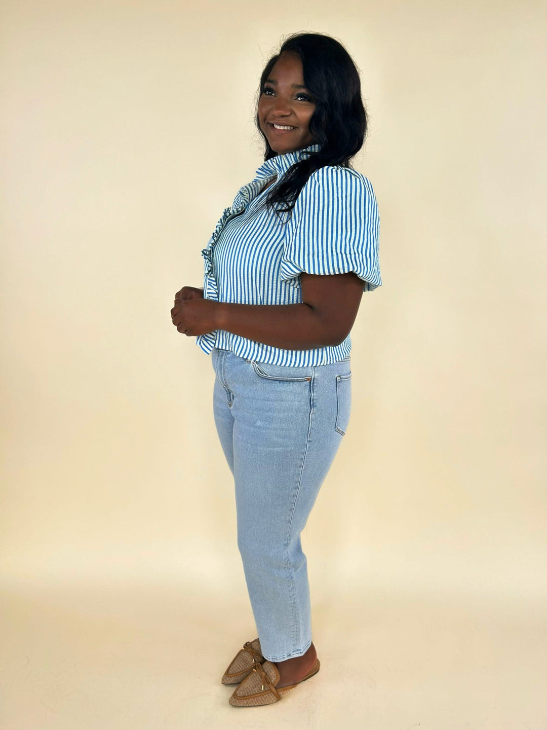 Side view of blue striped ruffle blouse with light wash denim jeans and neutral woven flats, casual spring outfit for women