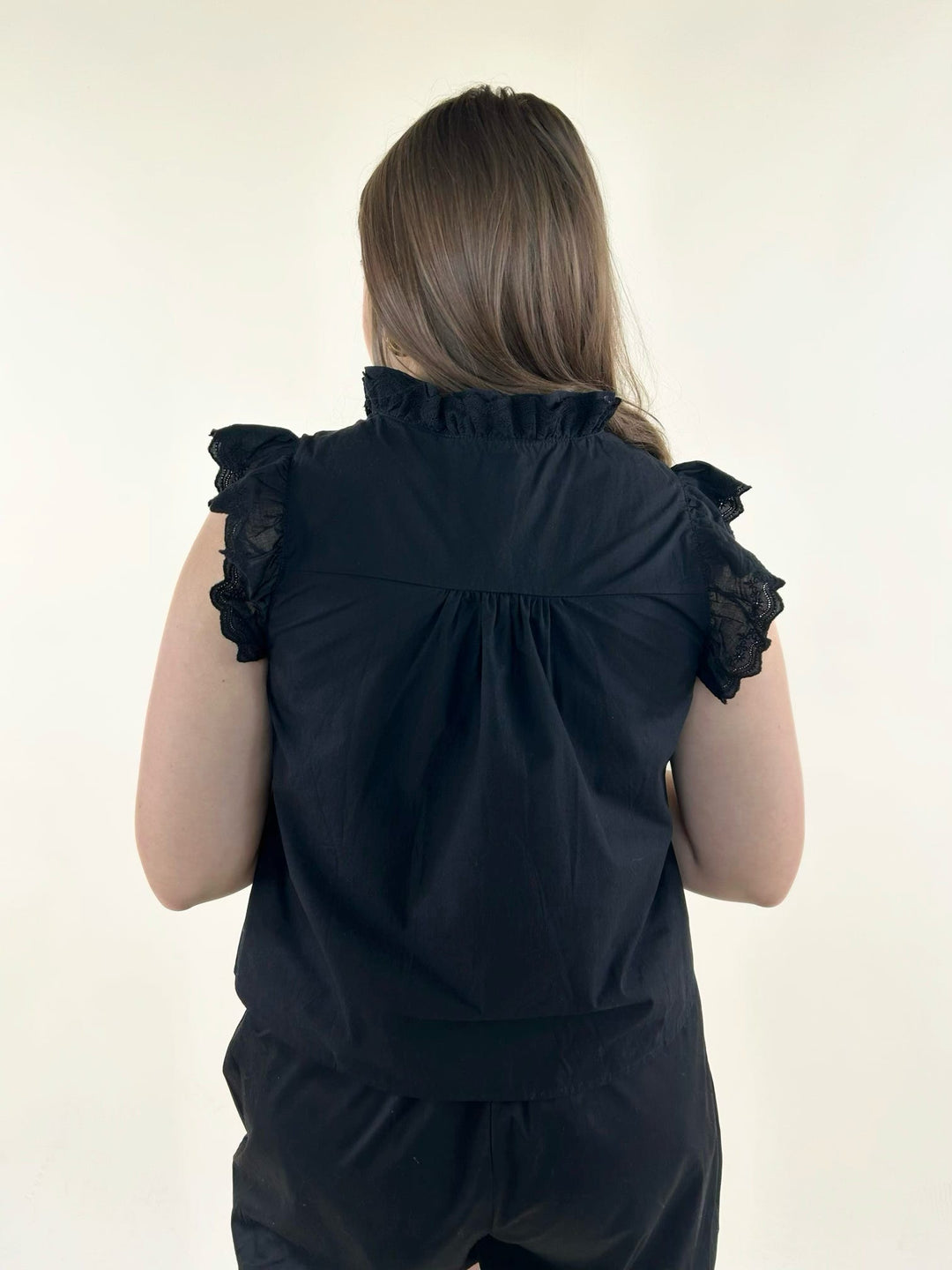 Back view of black ruffle neck blouse with gathered yoke detail, lace flutter sleeves, and elegant tailored styling