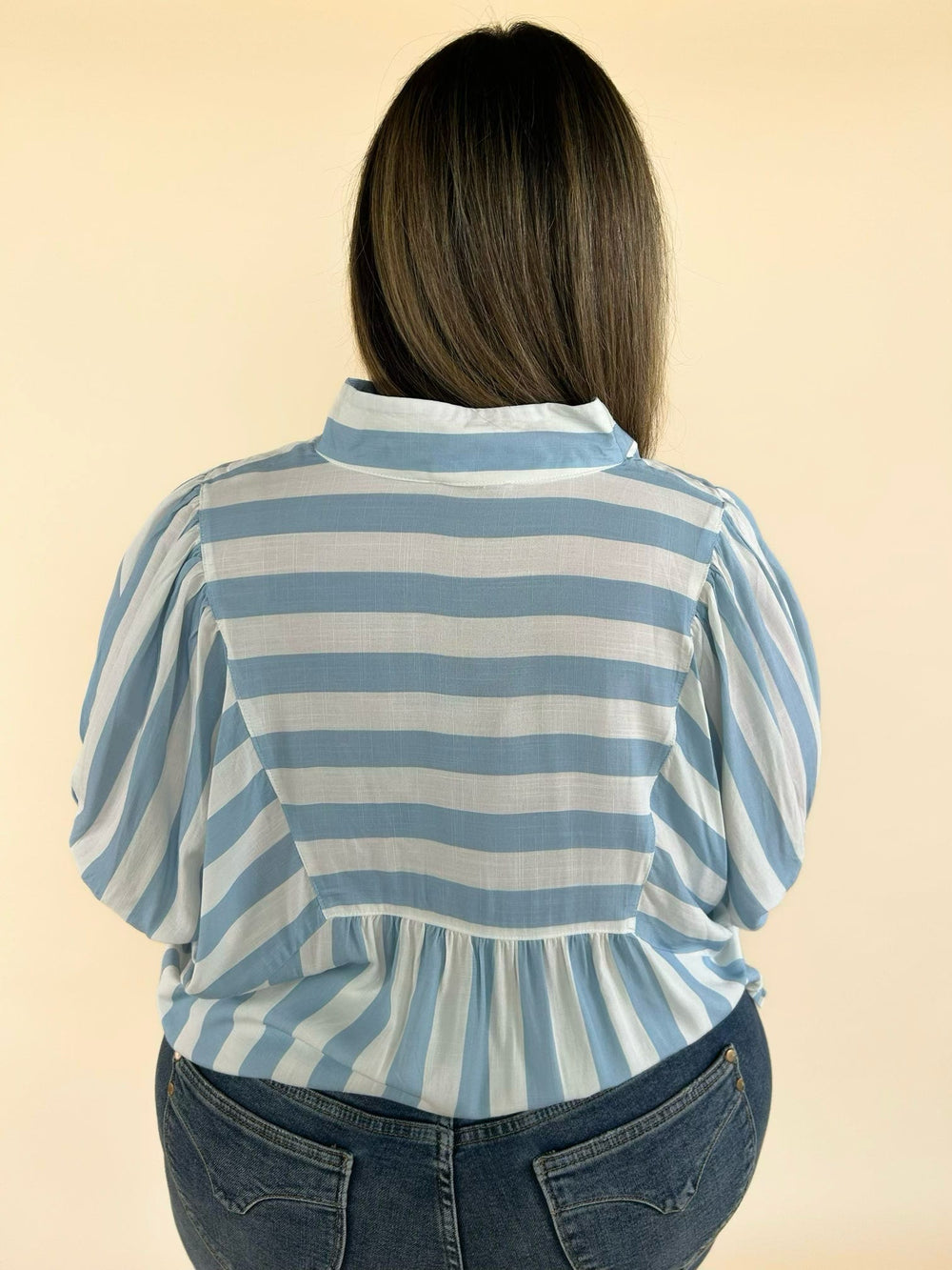 Back view of blue and white striped collared blouse with gathered yoke detail and puff sleeves