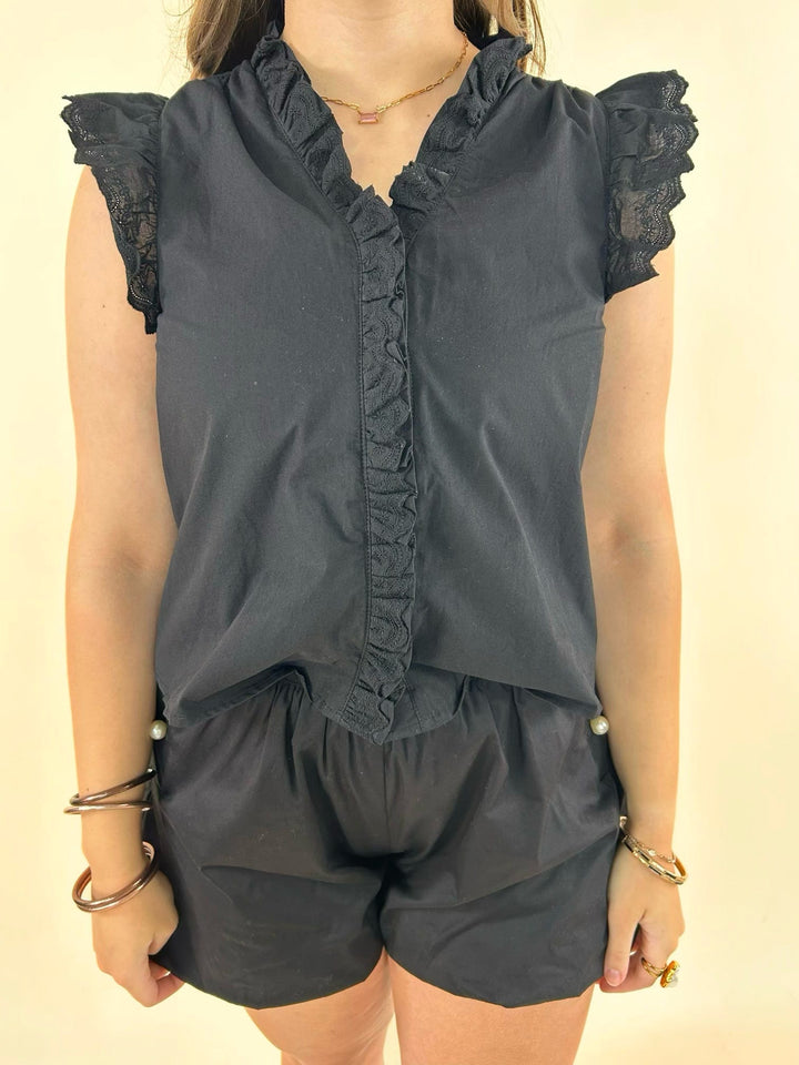 Close-up of black sleeveless blouse featuring lace ruffle trim, ruffled neckline, button-front placket, and feminine design details