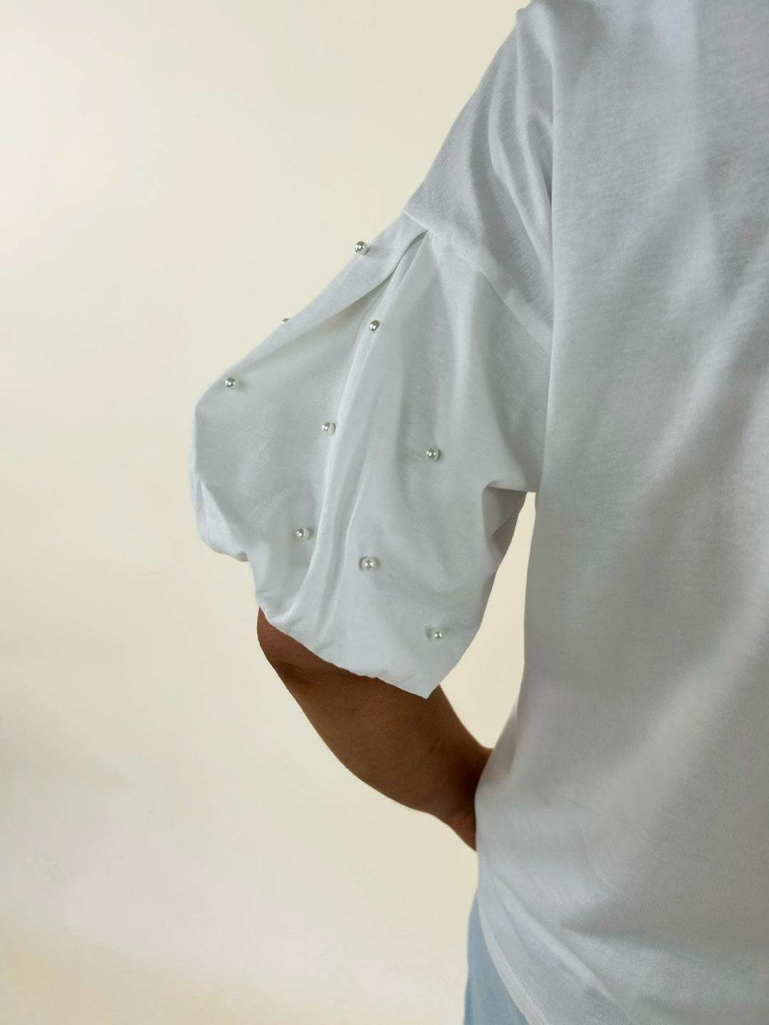 Close-up of white puff sleeve top featuring pearl embellishments, gathered sleeve detail, and feminine statement styling