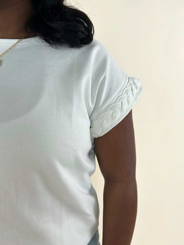 Close-up of white top featuring braided cuff sleeve detail, soft knit fabric, and elevated casual styling