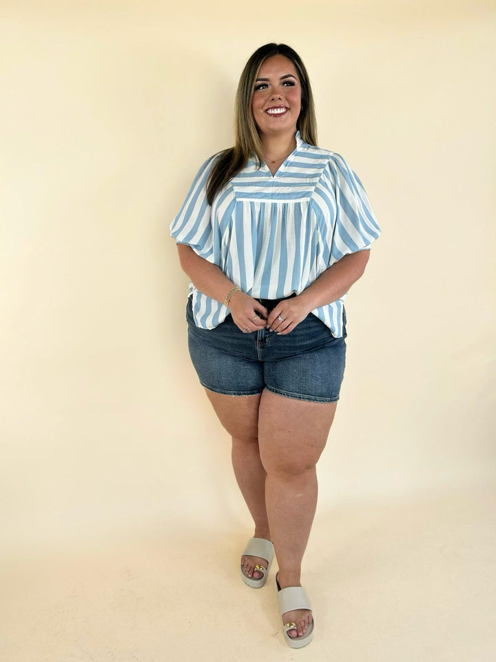 Women’s blue and white vertical stripe blouse paired with dark denim shorts, casual summer outfit