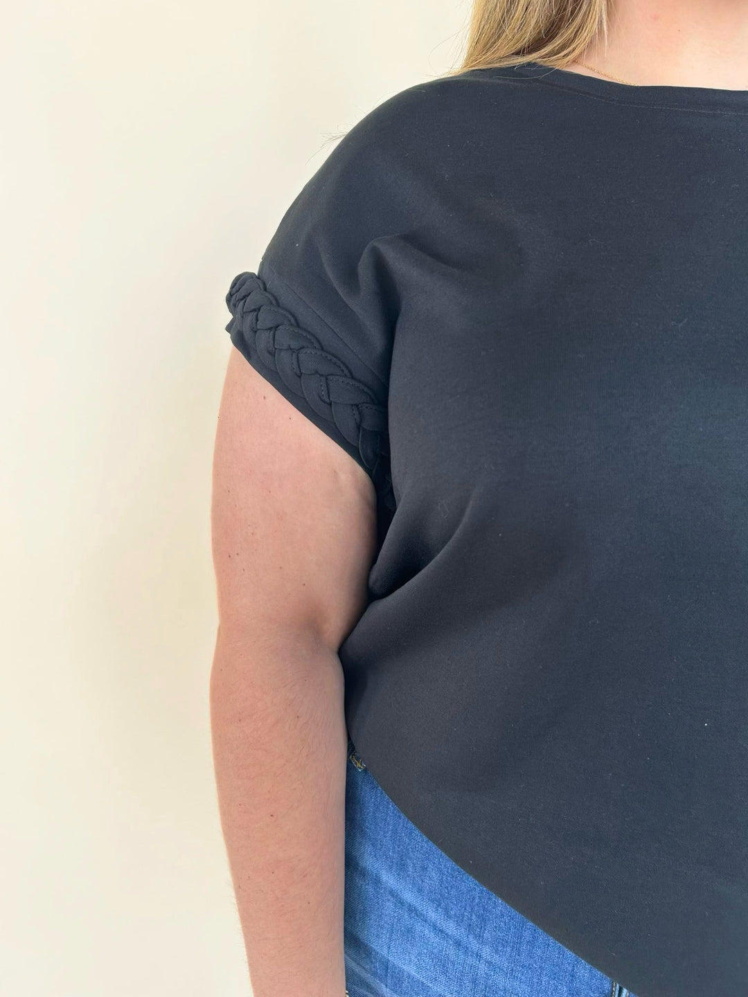 Close-up of black knit top featuring braided sleeve detail, cuffed short sleeves, and elevated casual design