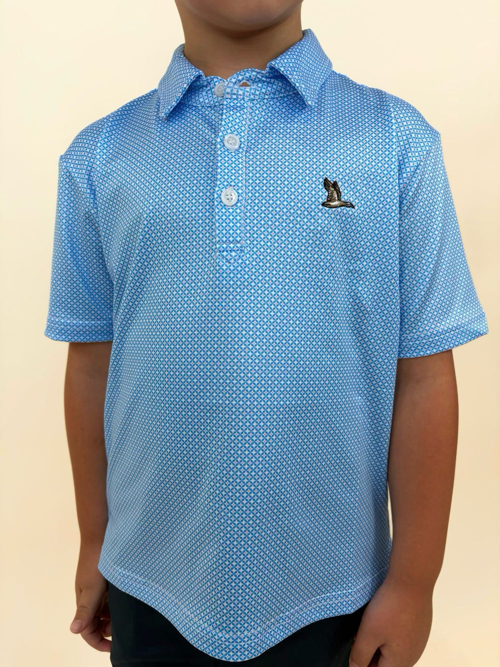 Roost Waterfowl boys performance polo close-up, blue geometric print polo shirt, embroidered flying duck logo, youth golf and outdoor apparel