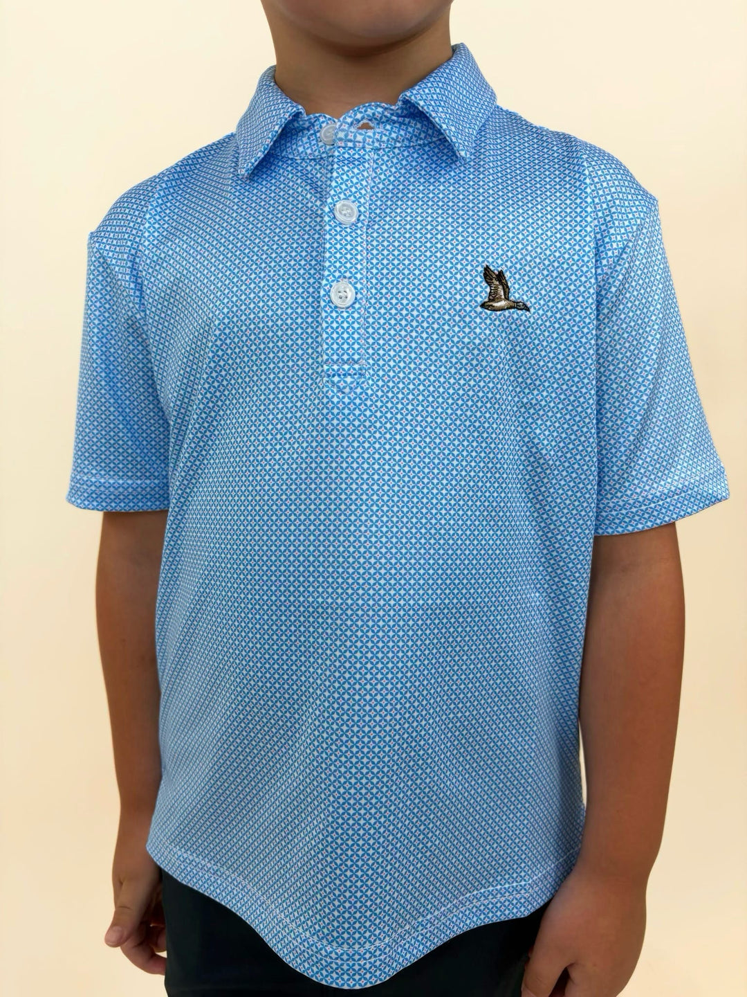 Roost Waterfowl boys performance polo close-up, blue geometric print polo shirt, embroidered flying duck logo, youth golf and outdoor apparel