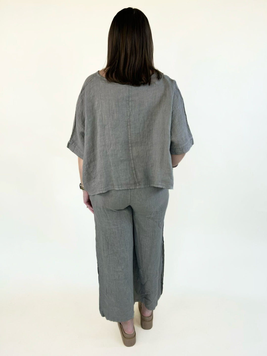 Mocha linen wide-leg pants with a relaxed fit, cropped length, breathable woven fabric, and decorative side button details, paired with a matching linen top.