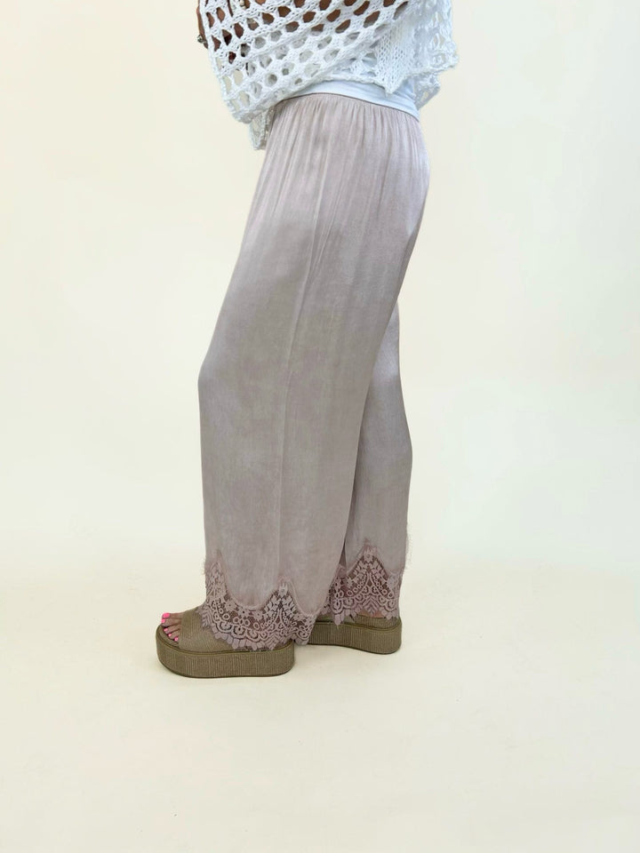 Blush satin wide-leg pants showcasing a soft drape, relaxed fit, elastic waistband, and intricate lace trim at the hem for an elegant finish.