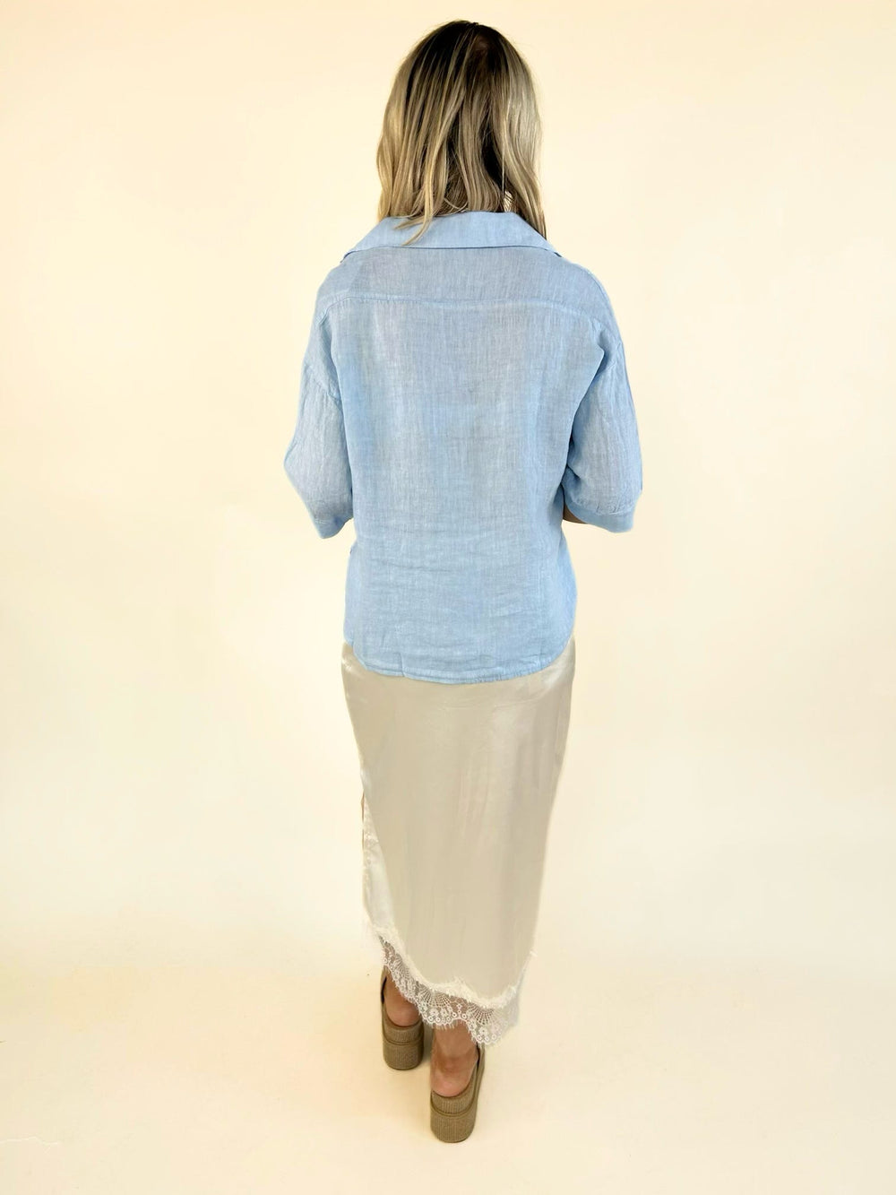 Back view of a women's light blue linen shirt featuring a relaxed fit, collared neckline, lightweight breathable fabric, and elbow-length sleeves.
