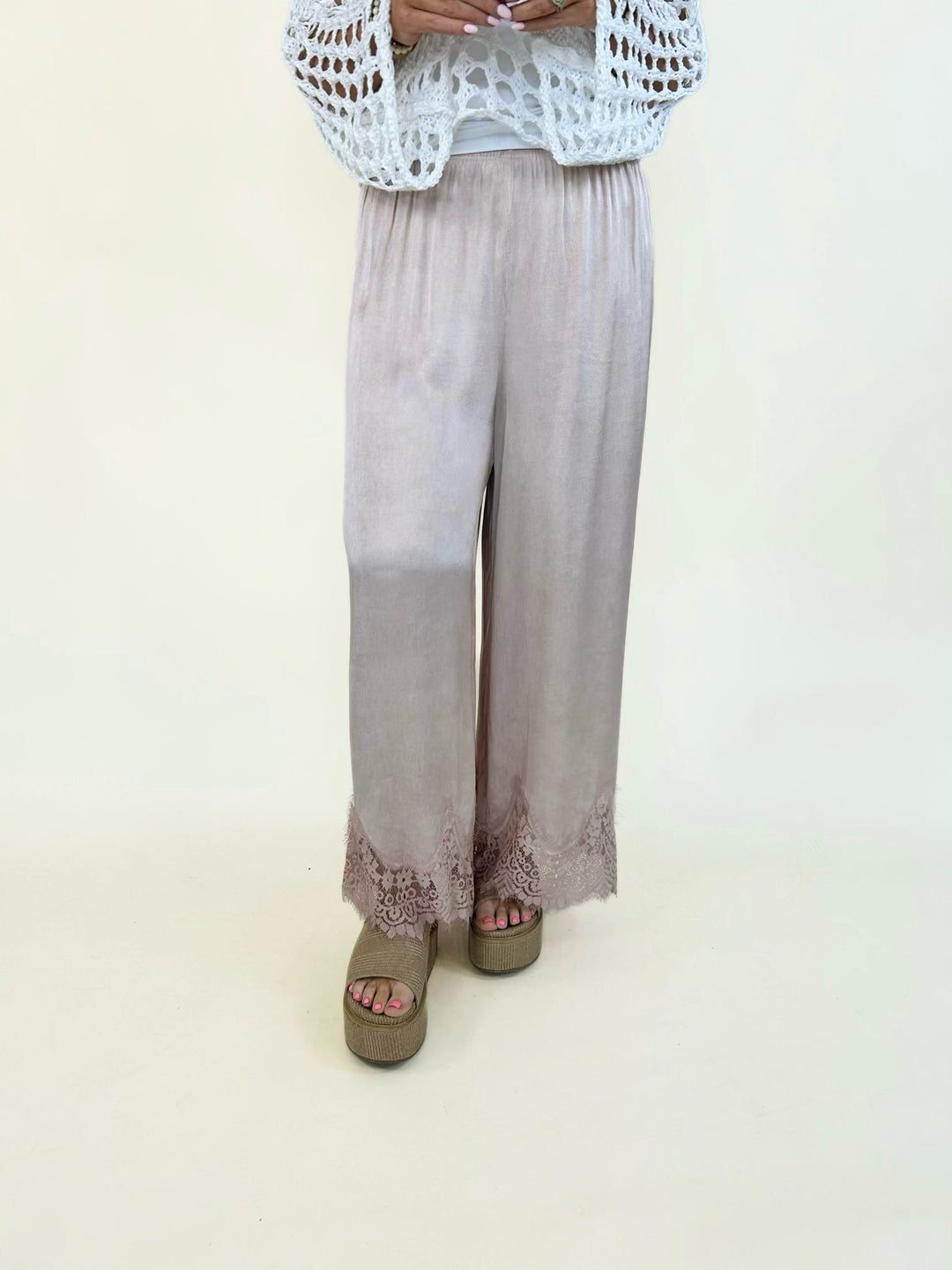 Blush satin wide-leg pants featuring a relaxed pull-on fit, elastic waistband, and elegant floral lace trim along the hem for a feminine, elevated look.