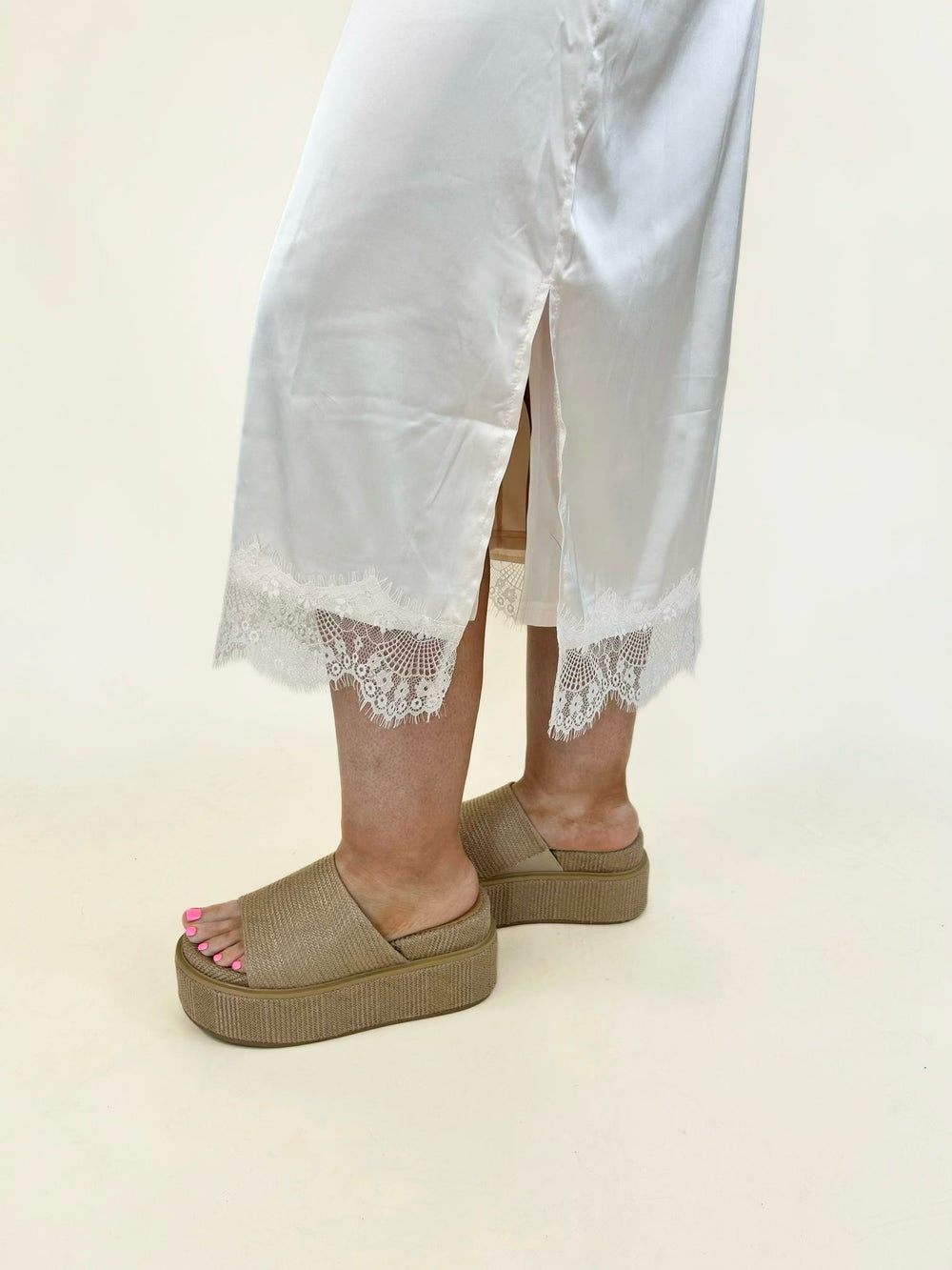 Cream satin midi skirt with a flowing silhouette, side slit, and intricate floral lace trim at the hem, offering an elegant and feminine look.