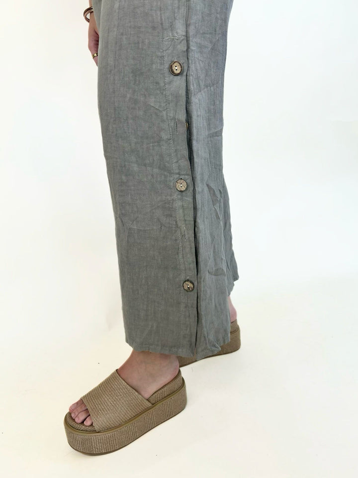 Close-up of mocha linen wide-leg pants showcasing decorative side buttons, side slit detail, breathable linen fabric, and a relaxed cropped leg.