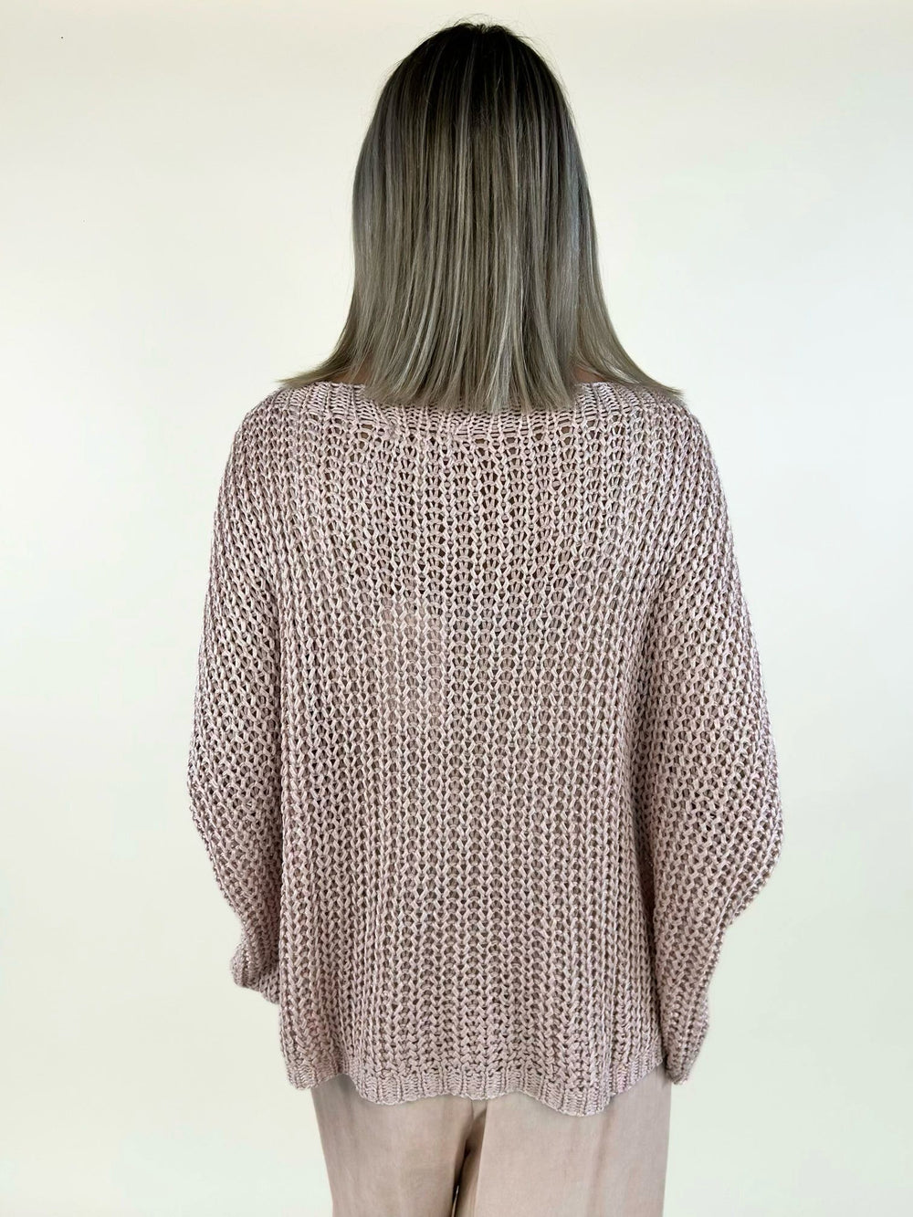 Back view of a blush pink open-knit oversized sweater featuring long drop sleeves, ribbed cuffs, and a relaxed silhouette paired with blush satin lace-trim wide-leg pants.