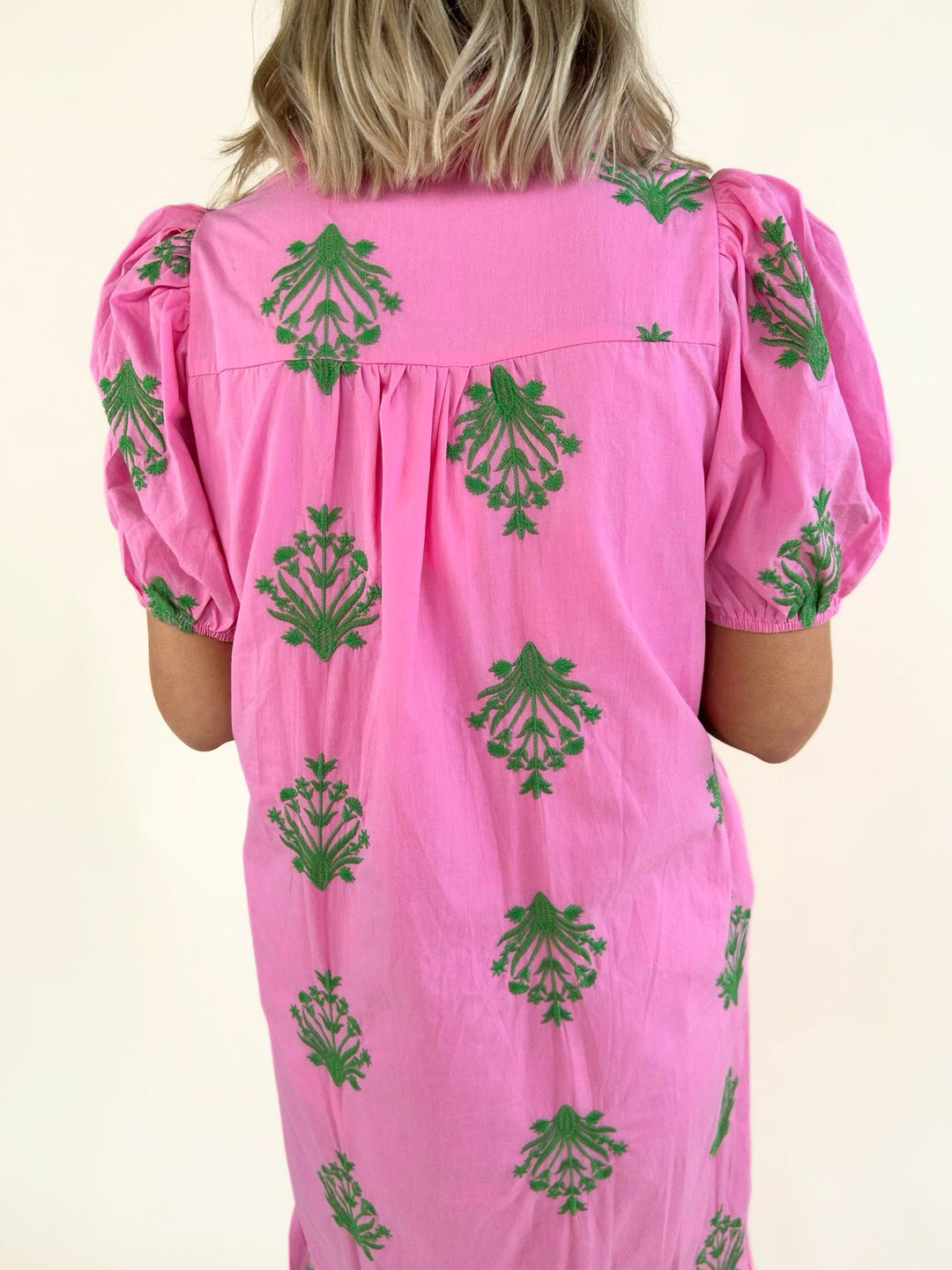 Close-up back view of a pink embroidered midi dress featuring green floral embroidery, puff sleeves, gathered back yoke, and lightweight woven fabric.