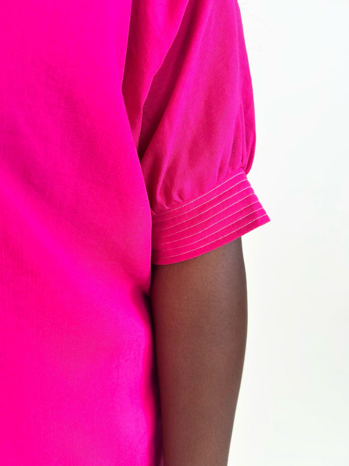 Close-up of the bright fuchsia blouse featuring the gathered short sleeve with stitched cuff detail and lightweight woven fabric.
