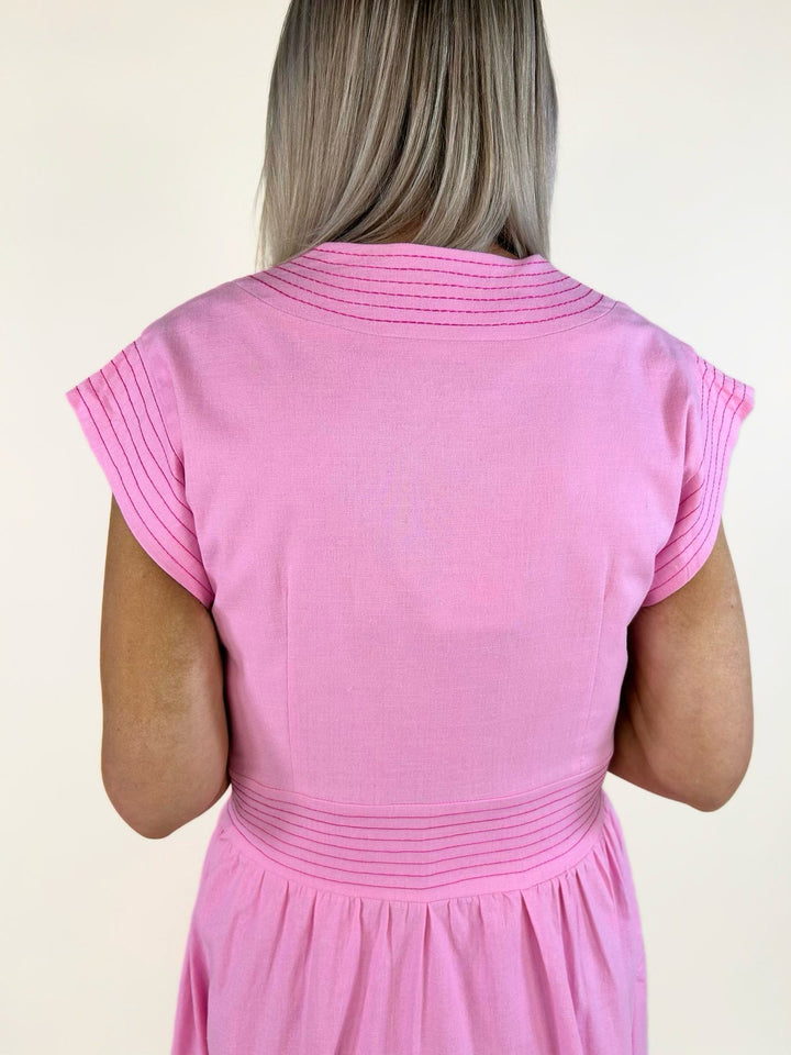 Close-up back view of the pink midi dress showcasing the fitted waist, decorative pintuck detailing across the shoulders and waist, and cap sleeves.