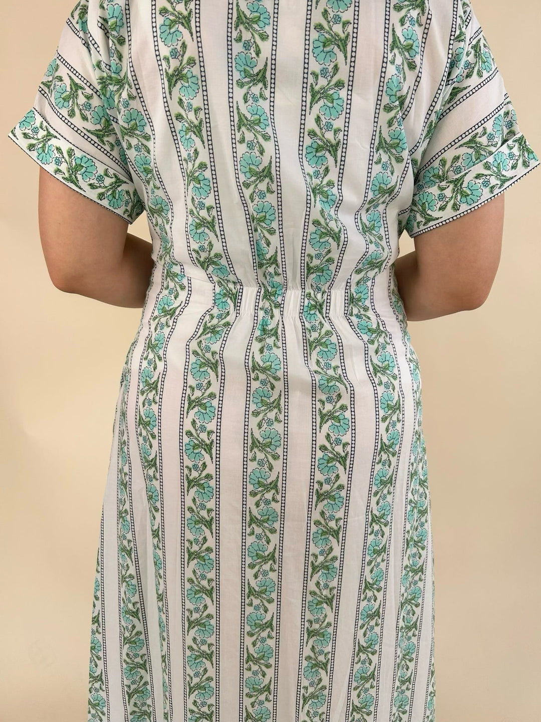 Close-up back view of the white midi dress featuring a green floral stripe print, short sleeves, and a fitted waist for a flattering silhouette.