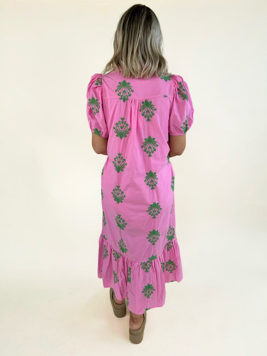 Back view of the pink embroidered midi dress showcasing green floral embroidery, puff sleeves, a relaxed silhouette, and a tiered ruffle hem.