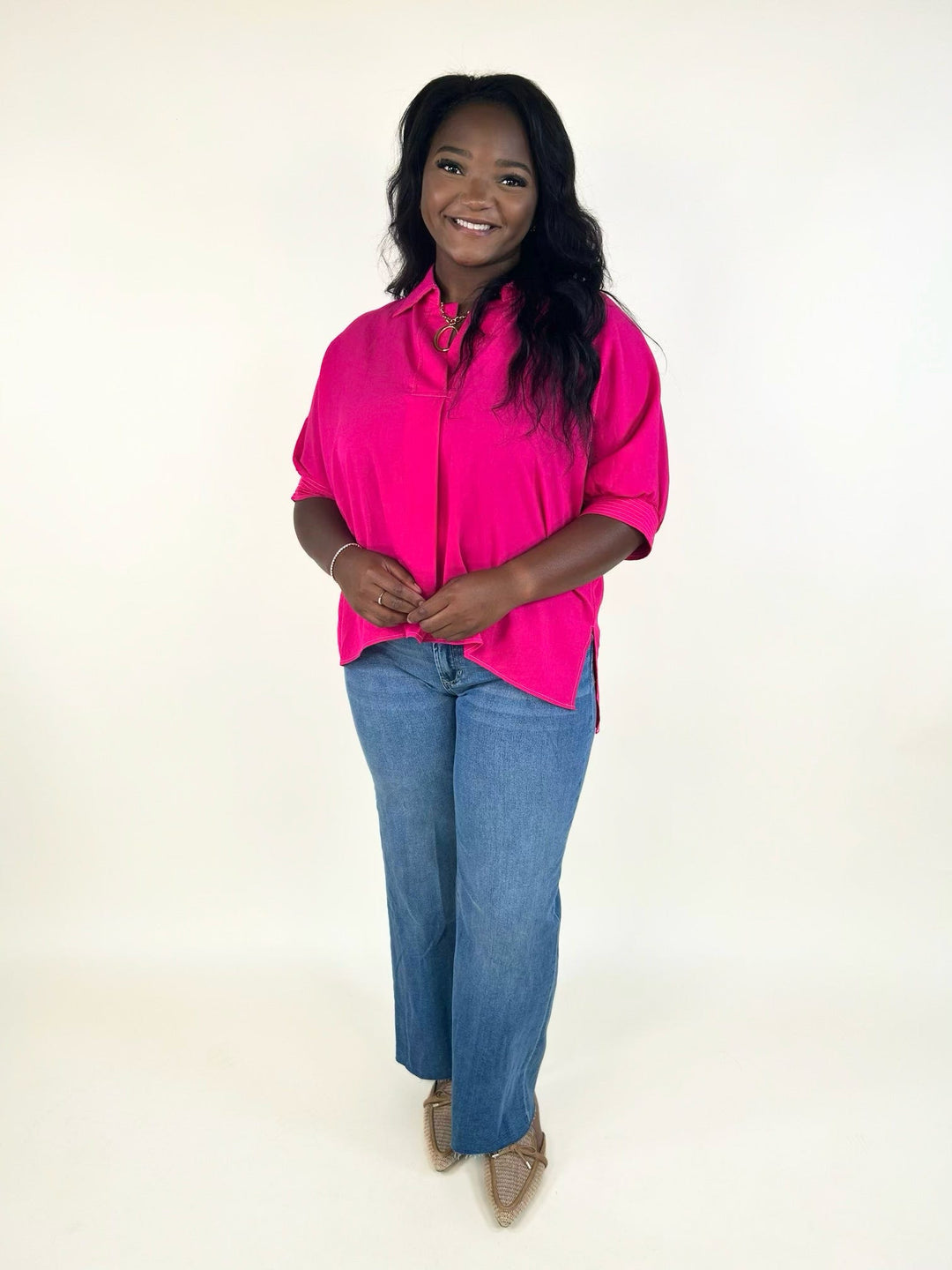 Front view of the bright fuchsia collared short sleeve blouse with a relaxed fit, side slits, split neckline, and wide leg light wash jeans.