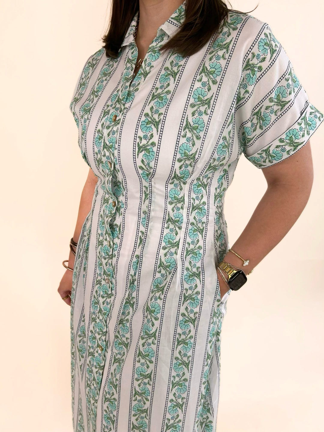 Side angle of the white collared floral stripe midi dress featuring a button-front design, fitted waist, short sleeves, side pockets, and lightweight woven fabric.