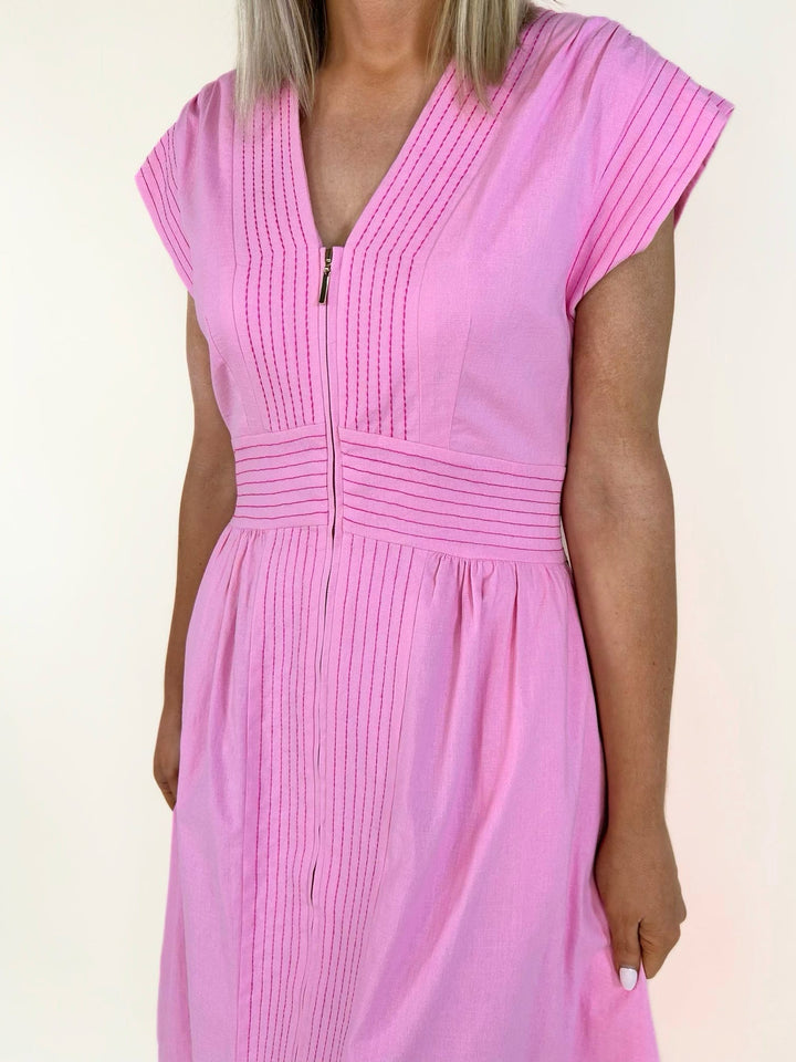 Close-up front view of the pink V-neck midi dress highlighting the front zipper, pintuck detailing, fitted waist, and lightweight woven fabric.