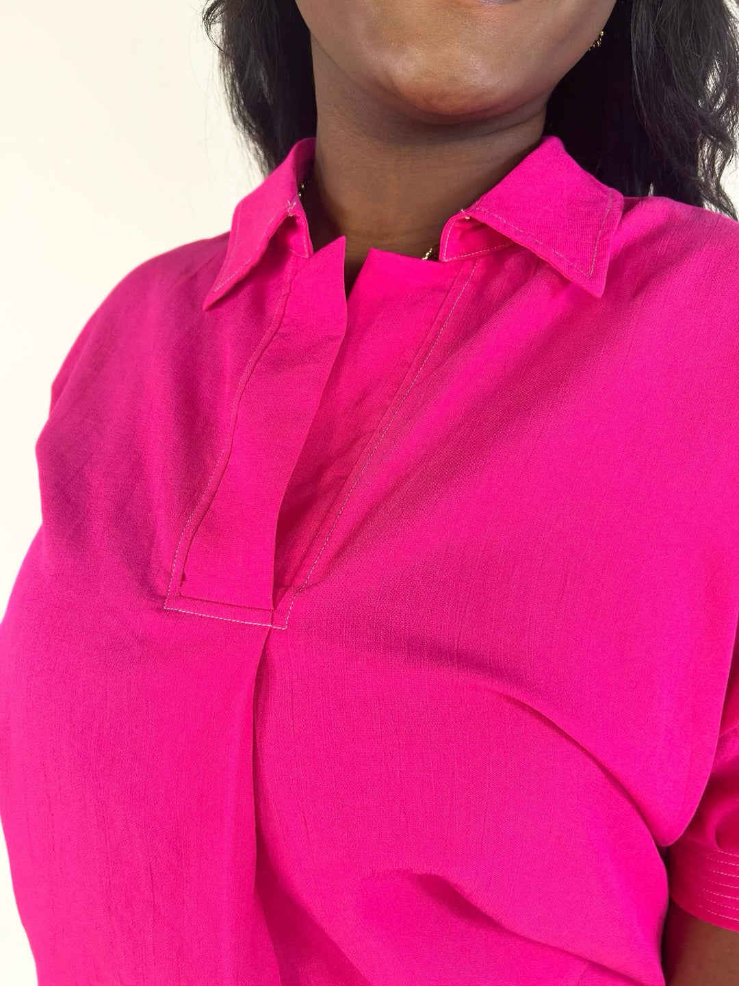 Close-up of the bright fuchsia blouse showcasing the collared split neckline, clean front placket, and lightweight textured woven fabric.
