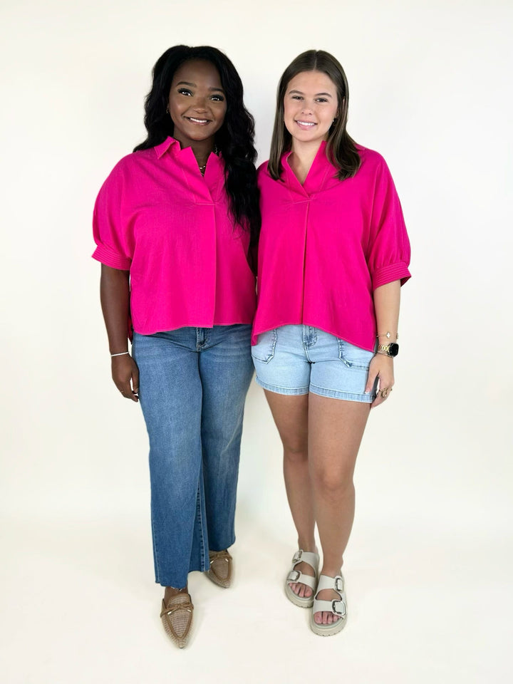 bright fuchsia collared short sleeve blouse featuring a relaxed silhouette, split neckline, cuffed sleeves, and lightweight woven fabric styled with denim.