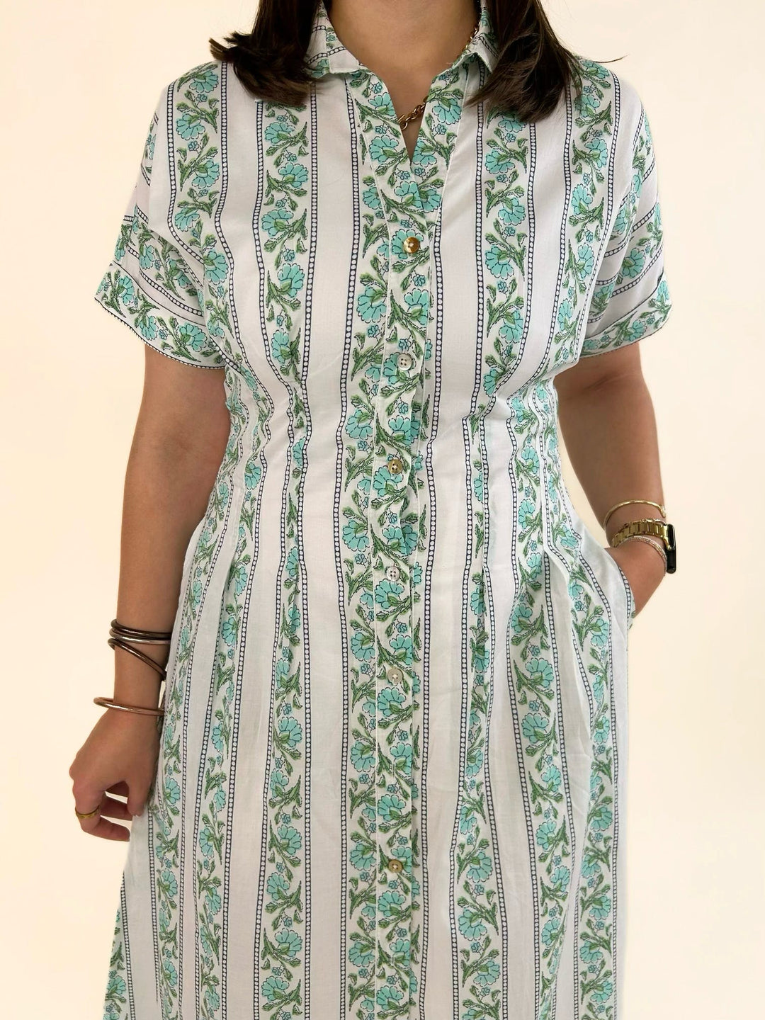 Close-up front view of a white collared button-front midi dress with a green floral stripe print, short sleeves, and a flattering fitted waist.