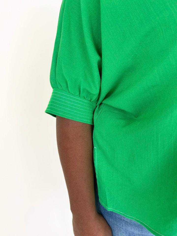 Close-up of the vibrant green blouse highlighting the gathered cuffed short sleeve, side slit hem, and lightweight textured woven fabric.
