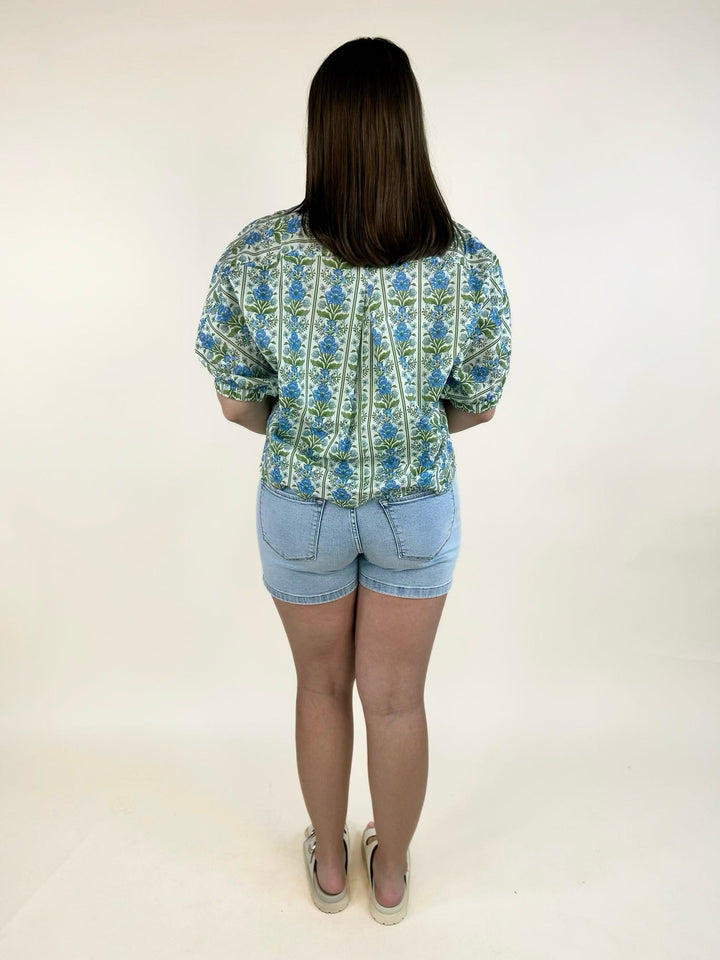 Back view of blue botanical floral print cotton blouse with elastic puff sleeves by Entro