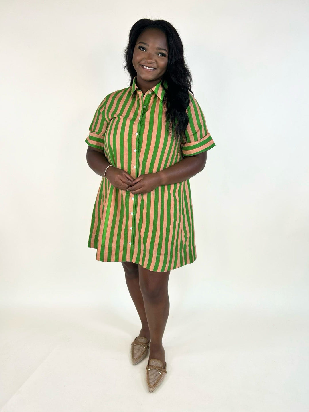 Model wearing the THML Weekend Getaway Striped Shirt Dress in green with peach vertical stripes, featuring a collared neckline, button-front closure, rolled short sleeves, side pockets, and a relaxed mini-length fit.