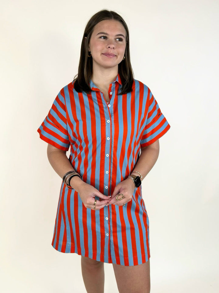 Front view of the THML Weekend Getaway Striped Shirt Dress in blue with orange vertical stripes, featuring a classic collared neckline, button-front design, rolled cuff short sleeves, relaxed fit, and breathable cotton construction.
