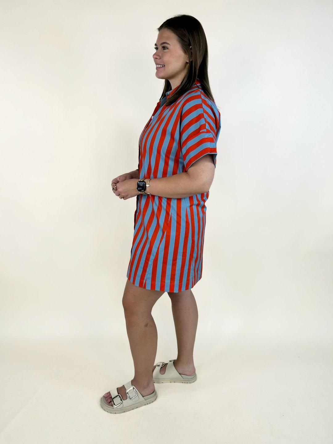 Side view of the THML Weekend Getaway Striped Shirt Dress in blue with orange vertical stripes, featuring a collared neckline, rolled short sleeves, relaxed fit, mini length, and lightweight 100% cotton fabric.