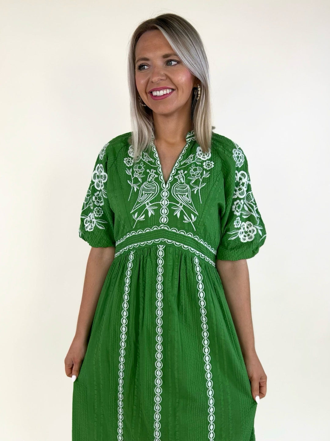 Close-up of emerald green embroidered dress with white floral and bird embroidery, split neckline, and puff sleeves