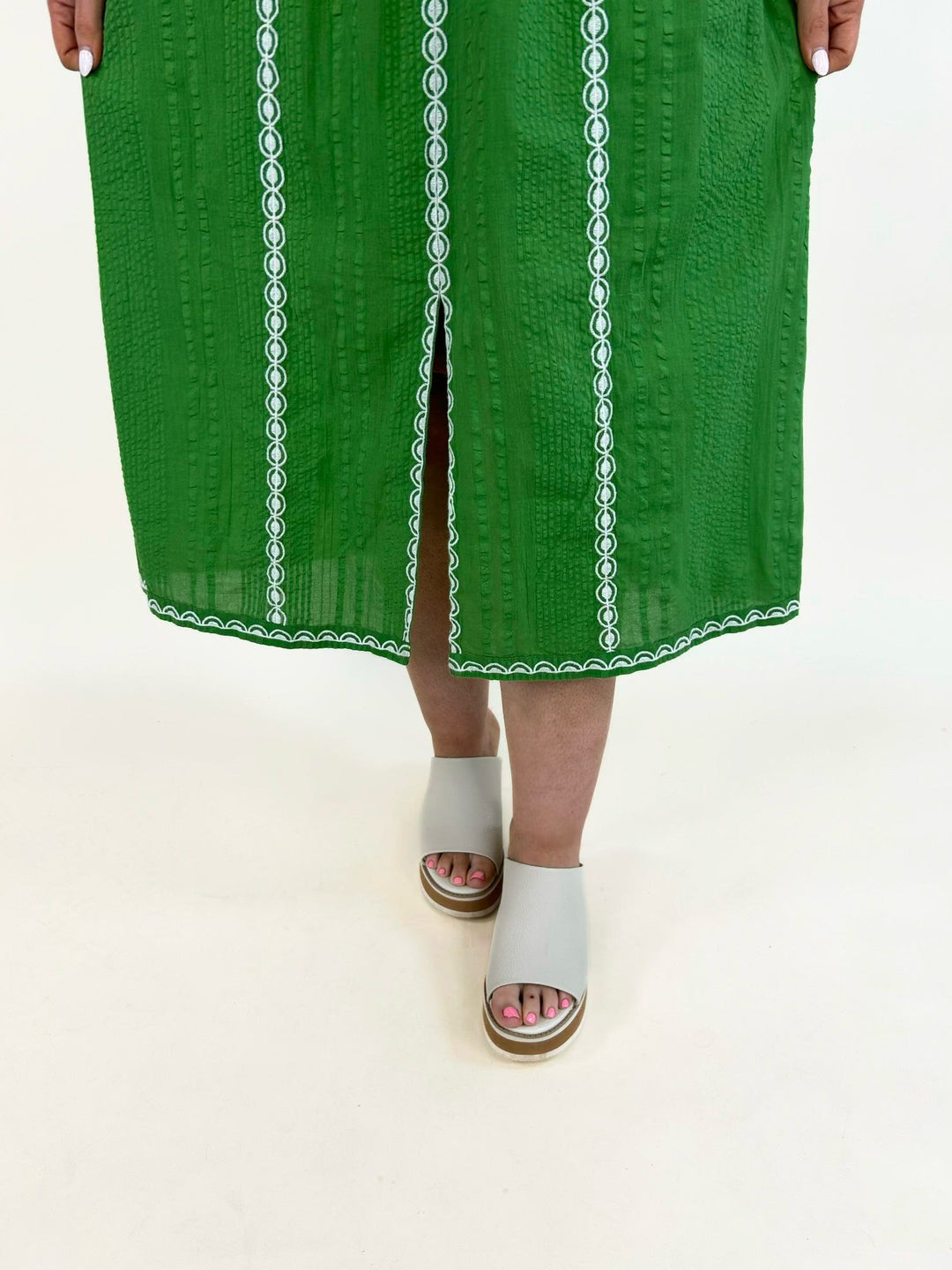 Close-up of emerald green midi dress hem featuring white embroidered trim and front slit detail
